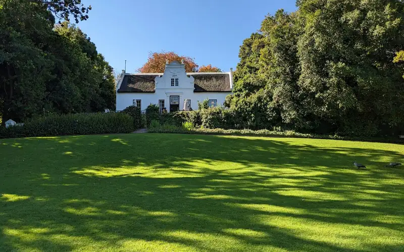 Groot gazon met schaduw van hoge bomen voor een wit huis
