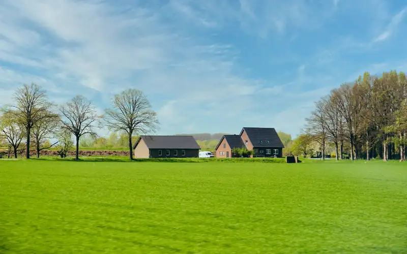 Zeer groot open grasveld onder een blauwe lucht met een huis in de verte